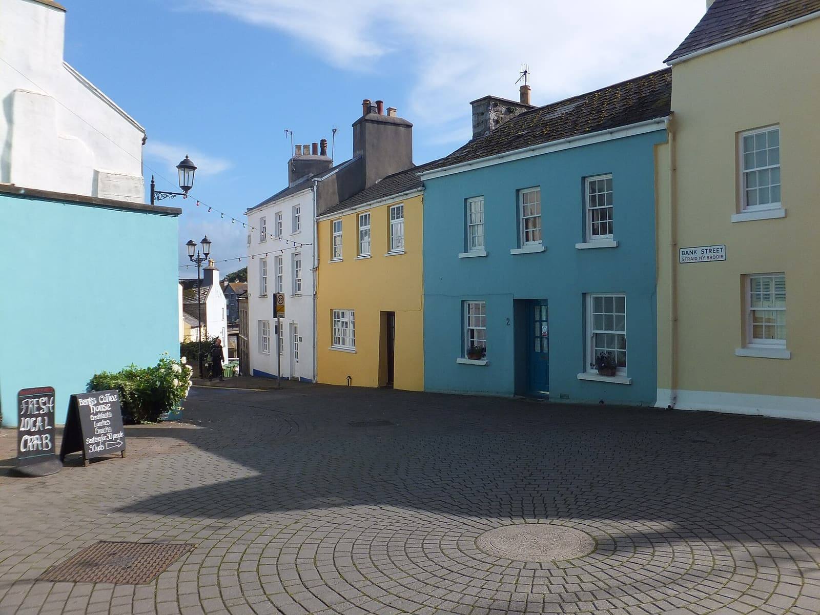 Brightly painted blue, yellow and white buildings along Bank Street in Castletown under a blue sky.