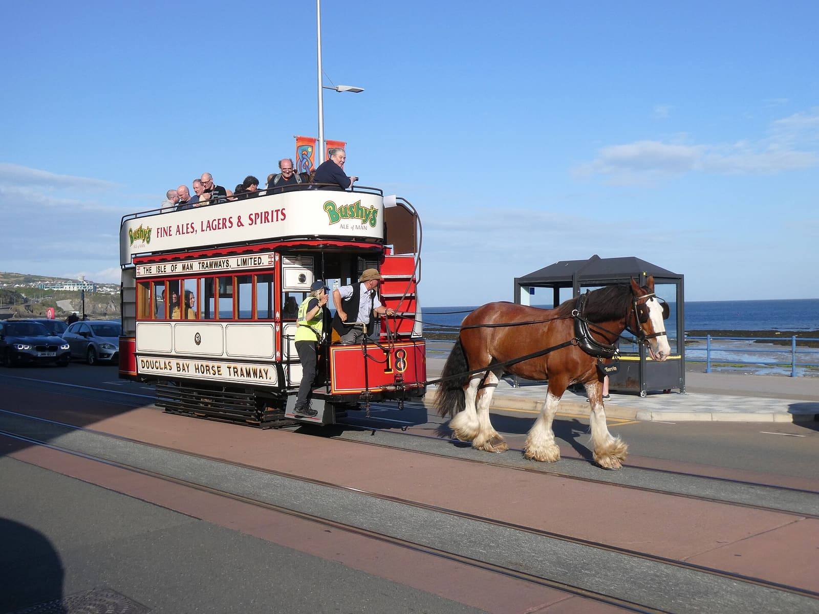 A horse-drawn open-top tram travelling along Douglas promenade beside the sea on a sunny day.