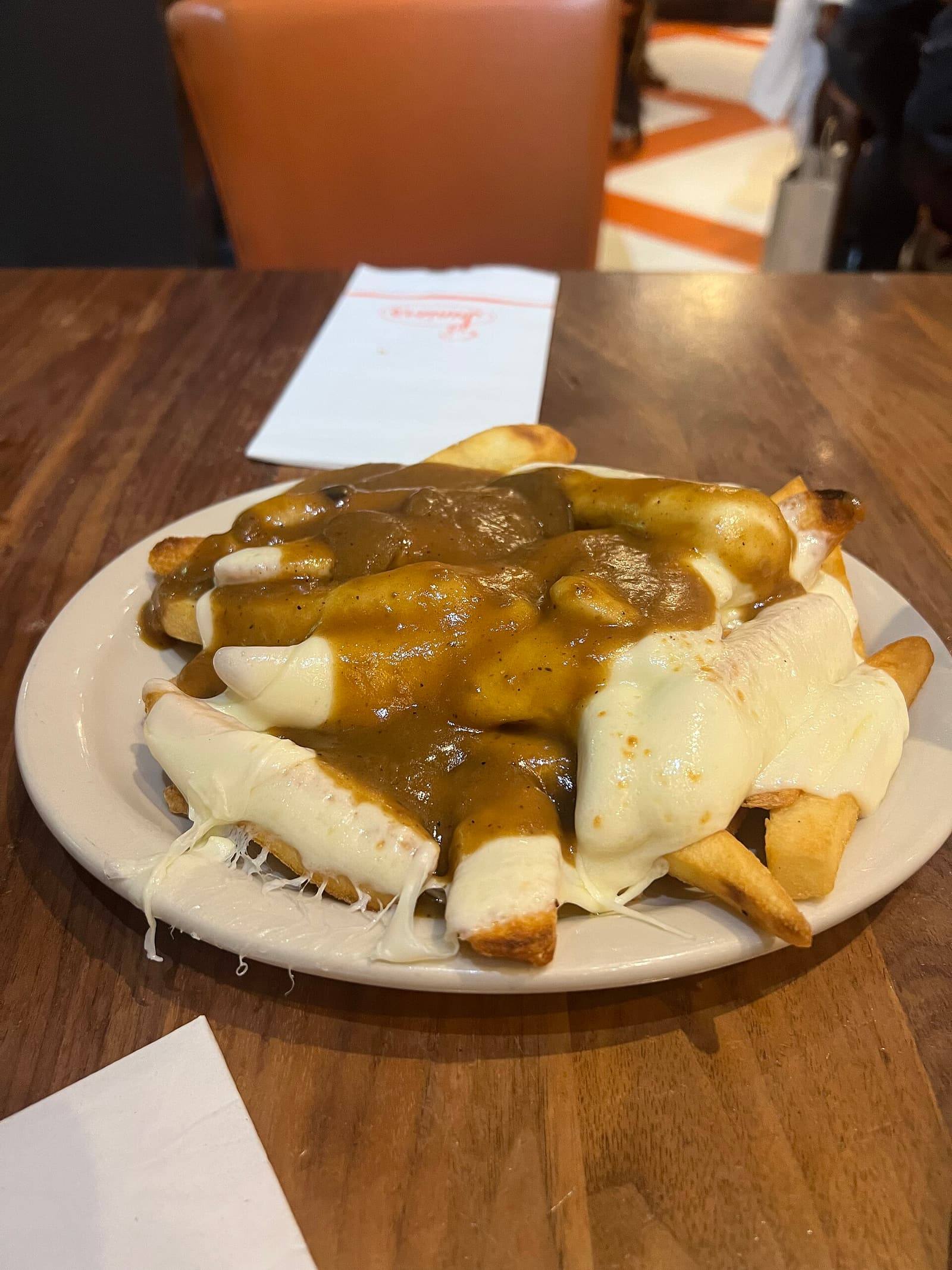 Thick-cut chips covered with melted white cheese and brown gravy on a white plate on a wooden table.