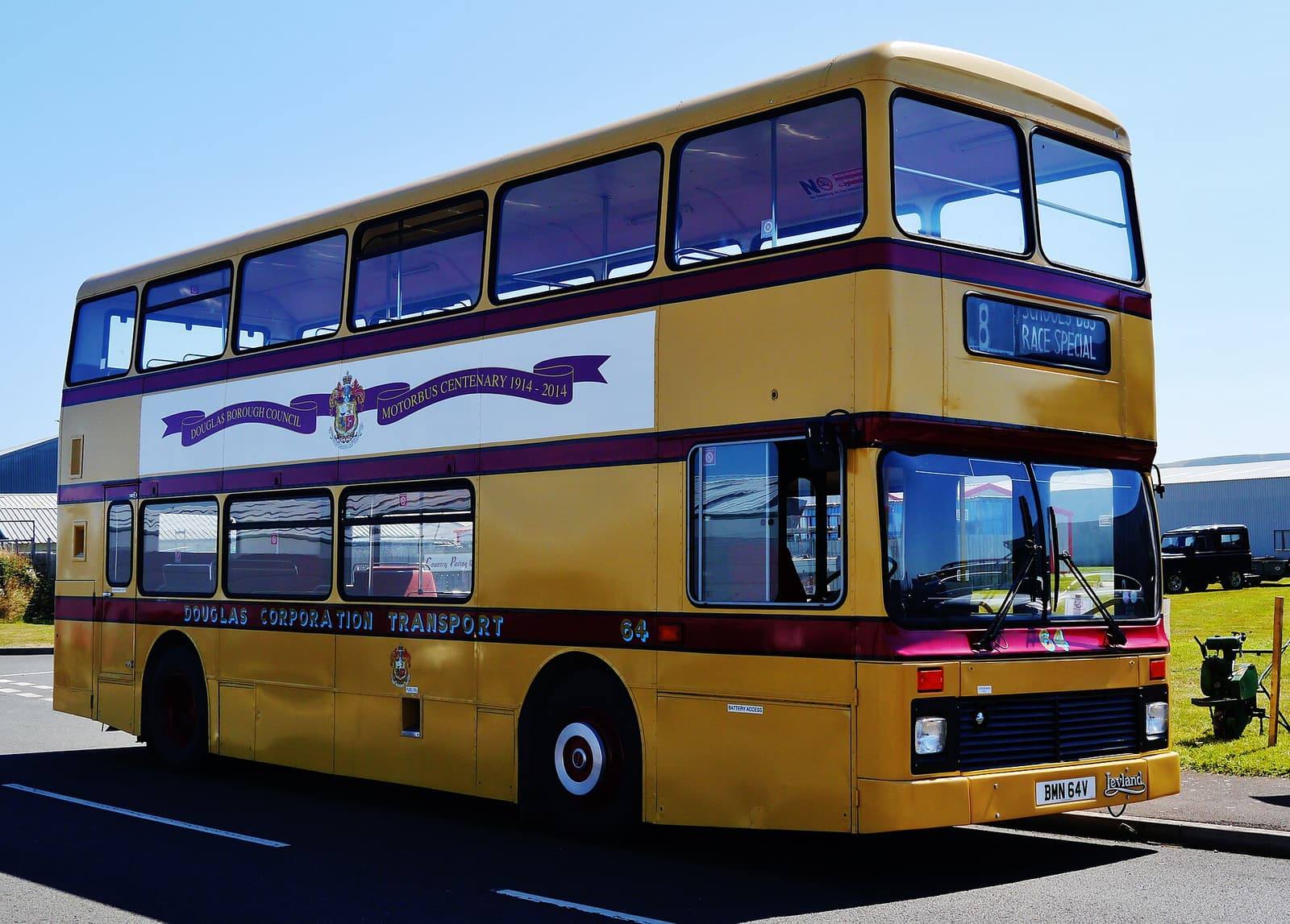 A yellow and maroon vintage Douglas Corporation double-decker bus parked outside the Jurby Transport Museum.