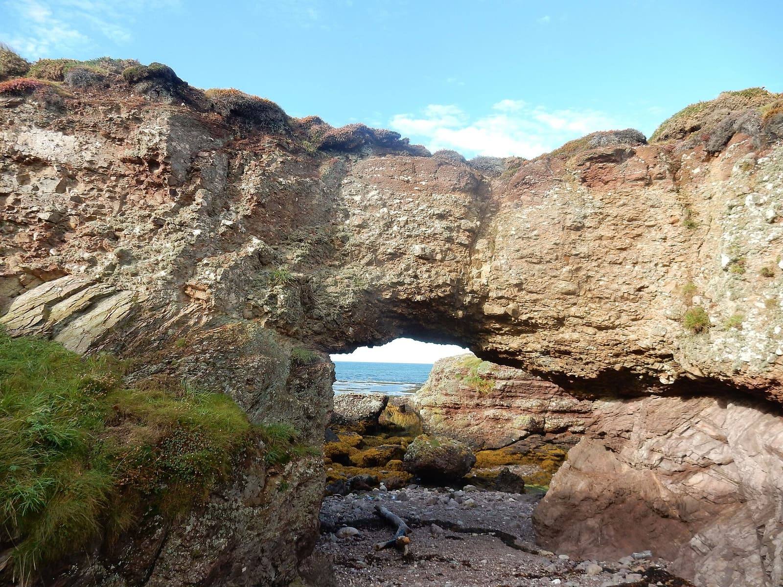 A natural rock arch on the shore at Langness, with the sea and blue sky seen through it.