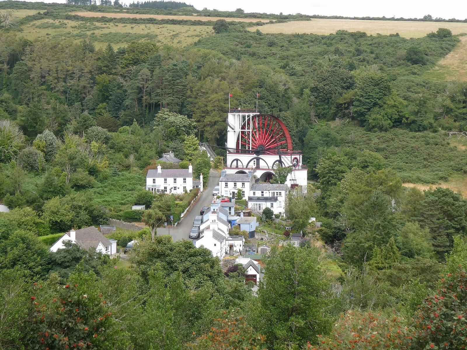 The Laxey Wheel among white houses and green woods in the Laxey valley, seen from the hillside above.