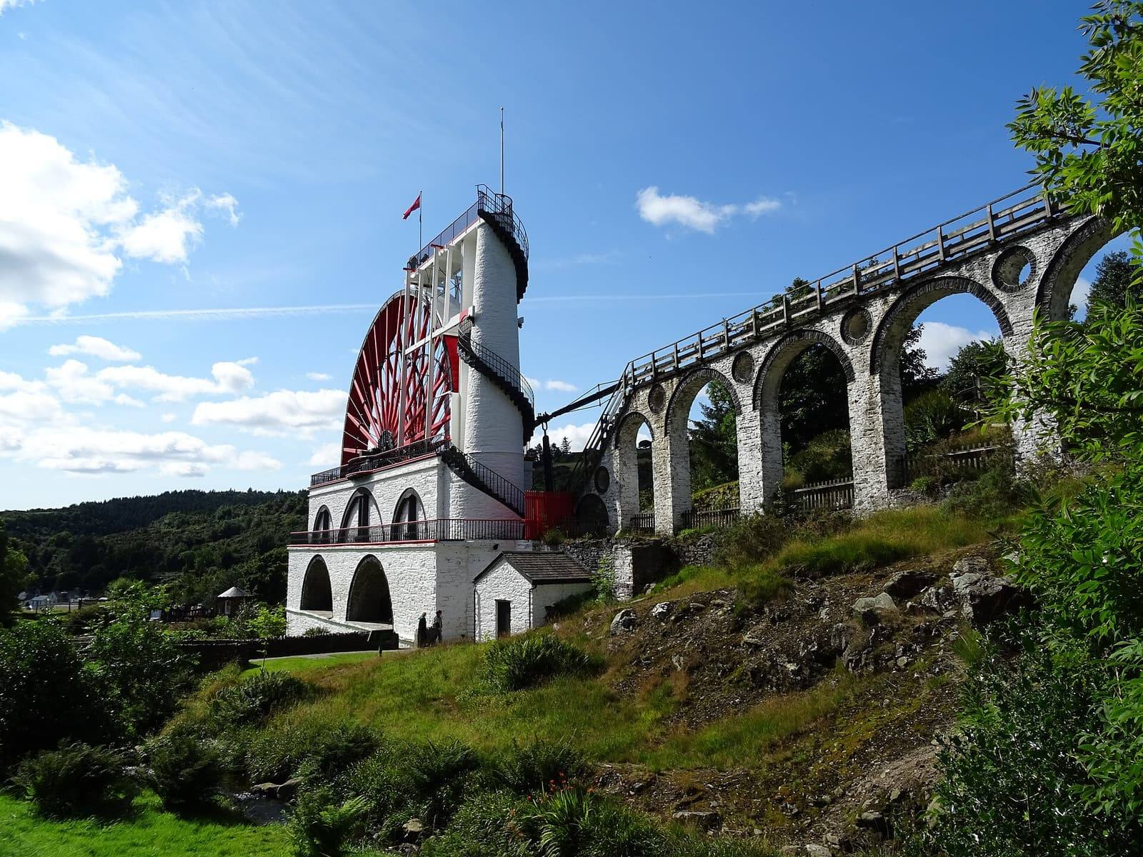 The great red waterwheel of Lady Isabella at Laxey and its white stone viaduct against a blue sky.