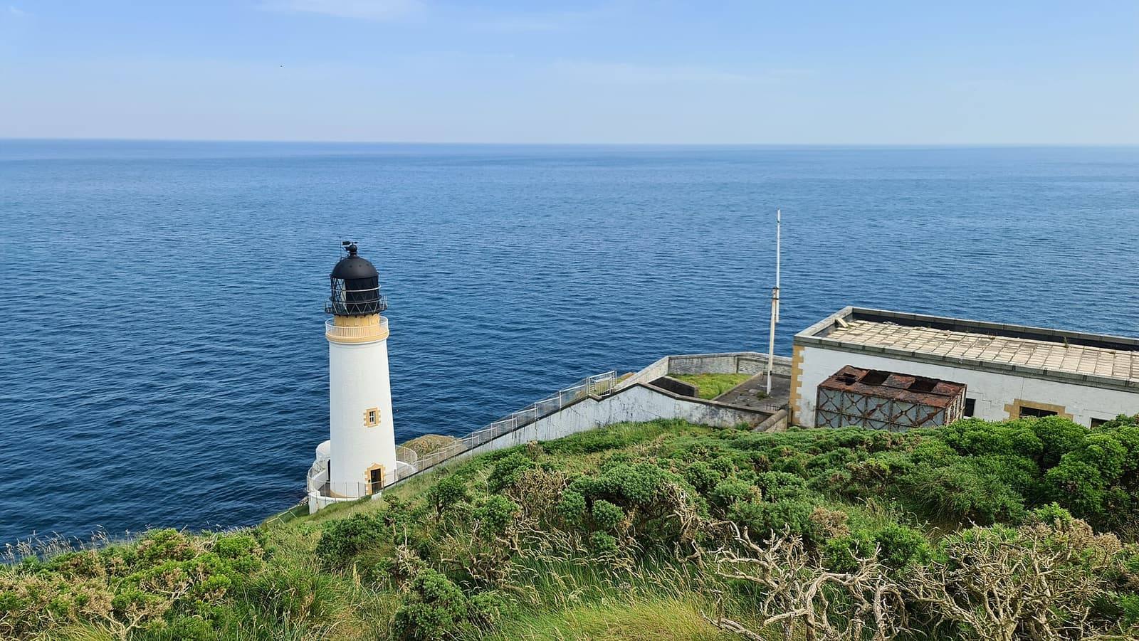 The white Maughold Head lighthouse on the green clifftop above a deep blue sea.
