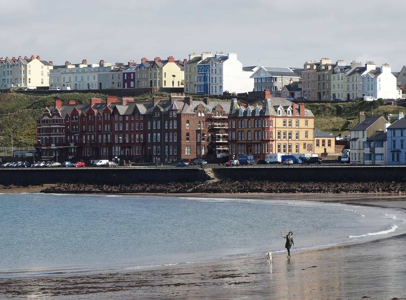 Colourful terraced houses and the red sandstone buildings of Peel's seafront above the beach and promenade.