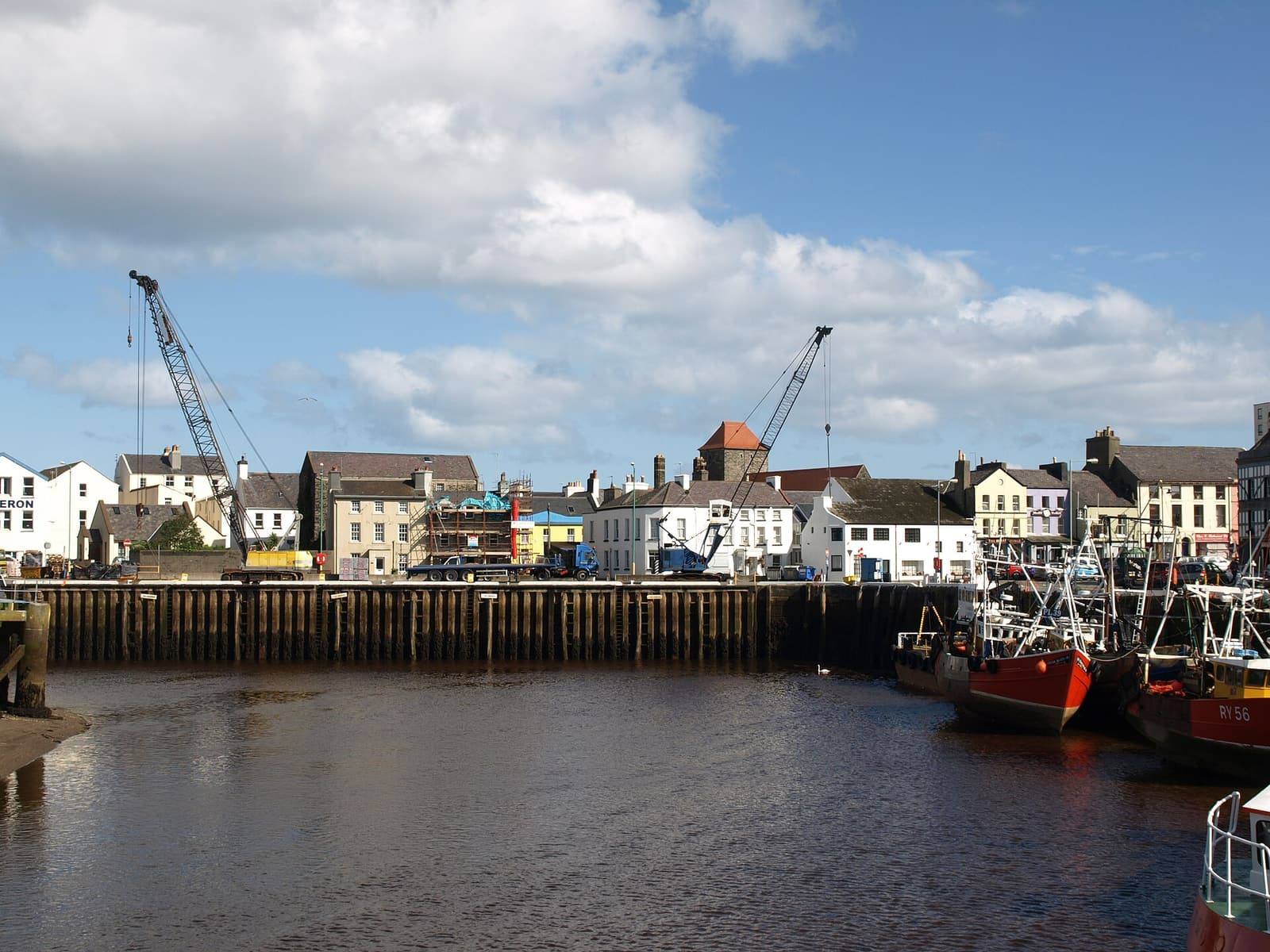 Red-hulled fishing boats moored in Ramsey harbour beside the quay under a bright, cloudy sky.