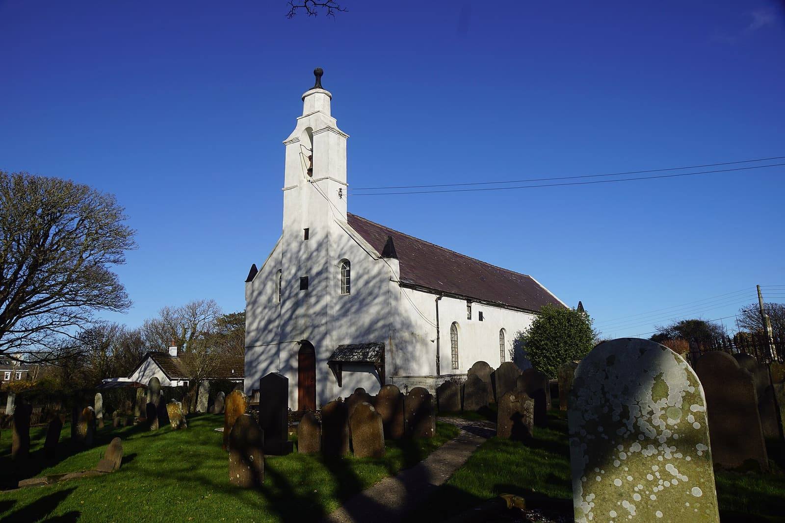 The white church at Santon with its tall bell tower against a deep blue winter sky, old gravestones in front.