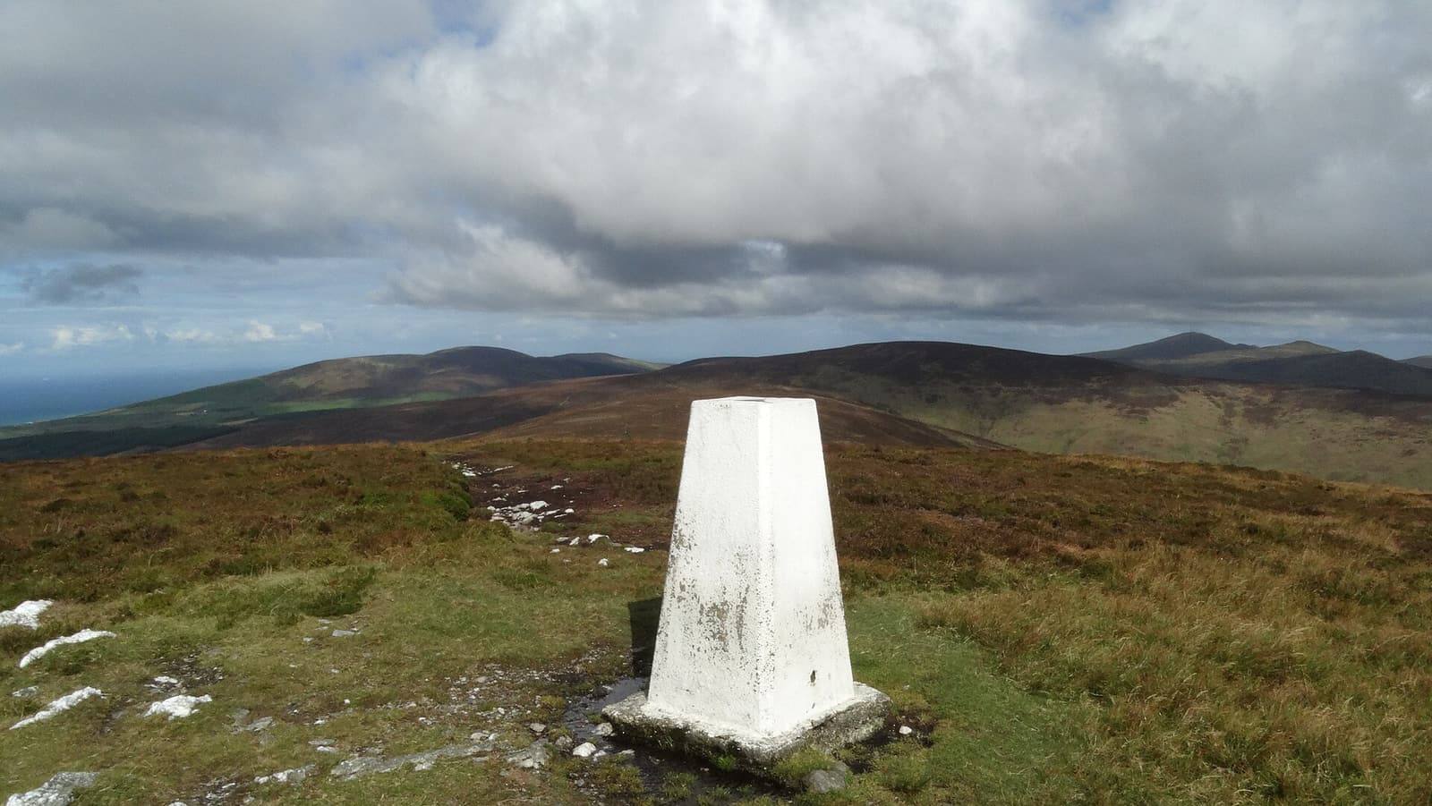 A white trig pillar on the heather-covered top of Slieau Ruy, with the central hills rolling away under cloud.