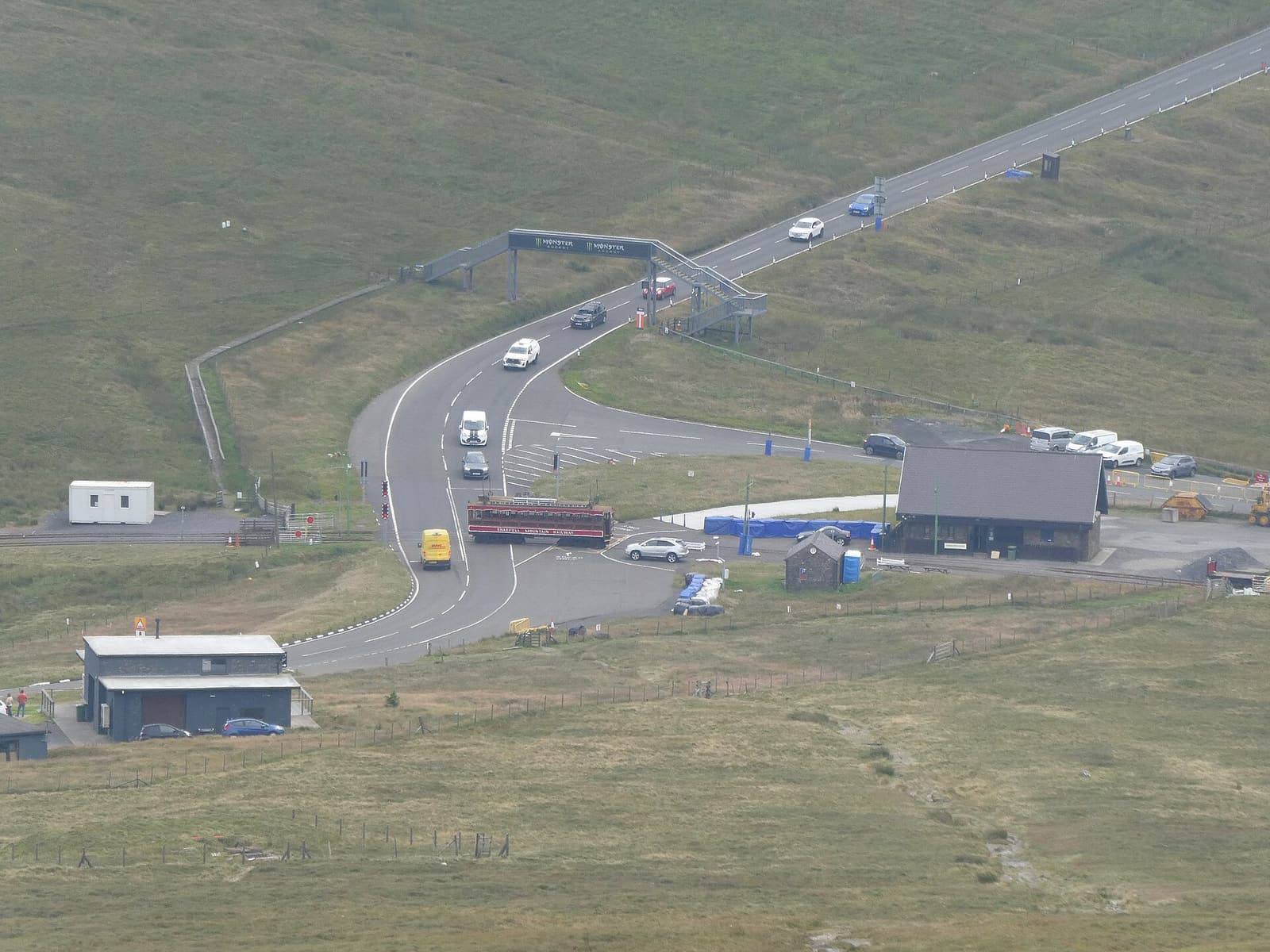 The Mountain Road winding past the Bungalow on the open moorland below Snaefell, seen from the hillside above.